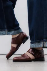 Zapato bajo de cuero negro, estilo monk strap con dos hebillas ajustables sobre el empeine. Presenta detalles de brogue (perforaciones) en la puntera y alrededor del borde superior. Tiene un taco bajo y ancho.