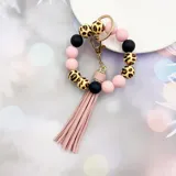 Llavero pulsera con cuentas de silicona en color rosa claro, negro y animal print de leopardo. Incluye un dije de flecos de cuero sintético rosa claro y un aro metálico dorado con mosquetón.