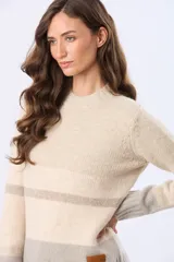Buzo tejido de tacto suave con diseño de rayas horizontales en tonos beige claro, beige oscuro y gris. Tiene cuello redondo y terminaciones acanaladas.