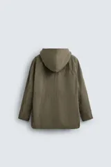 Parka color verde militar de corte amplio, confeccionada en tejido técnico ligero. Cuenta con cuello alto con capucha ajustable, cierre frontal con botones, mangas largas con puños ajustables, bolsillos de plastrón con solapa en la parte delantera, cintura ajustable con cordón y bajo con aberturas laterales ajustables con cordón.