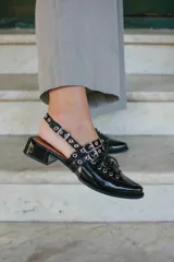 Sueco de cuero negro con cordones, ojales, hebillas y tira trasera regulable con elástico. Tiene taco cuadrado bajo.