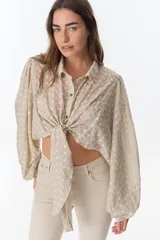 Camisa color beige con bordado de flores blancas, corte crop y mangas largas abullonadas. Se ata en la parte delantera.