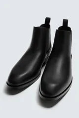 Bota estilo Chelsea de cuero negro, con punta fina, elásticos laterales y tirador trasero. Posee suela con ligero tacón.