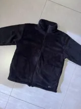 Buzo negro de poliéster con textura de sherpa y cierre frontal.