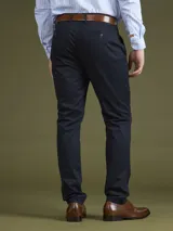 Pantalón de vestir azul marino, de corte slim fit, con bolsillos laterales y traseros. Se ajusta a la cintura con cinturón de cuero marrón.
