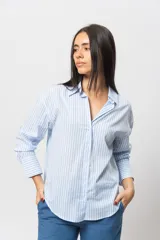 Camisa celeste a rayas verticales blancas, de corte recto y mangas largas con puños abotonados.