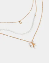 Collar corto multicadena dorada con una cadena de eslabones, una de perlas y una de eslabones con dije de flor blanca.