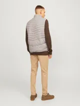 Chaleco puffer gris con cuello alto y cierre frontal con cremallera. Tiene bolsillos laterales y diseño acolchado horizontal.