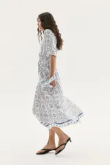Vestido midi con estampado floral en tonos celeste y azul, cuello camisero, botonadura frontal, mangas cortas raglán, elástico en la cintura y cinturón extraíble para atar.