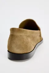 Zapato plano tipo mocasín color marrón claro, confeccionado en piel de serraje. Tiene copete subido, antifaz y punta redonda.