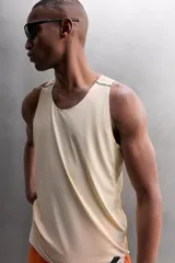 Camiseta deportiva sin mangas color beige, confeccionada en tejido técnico ligero y elástico con estructura perforada. Tiene cuello redondo amplio, sisas con acabados termofijados, bajo con aberturas laterales y logo estampado.