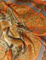 Pañuelo cuadrado de satén color naranja con estampado de motivos florales y grecas en tonos dorados, marrones y beige.
