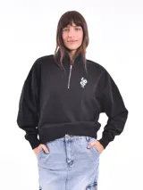Buzo negro de corte cropped con cuello alto y cierre metálico plateado hasta el pecho. Tiene un pequeño bordado blanco con forma de serpiente en el lado izquierdo del pecho.