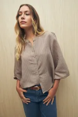 Camisa color beige con rayas verticales negras, cuello mao, mangas 3/4 abullonadas con puños elásticos y cierre frontal con botones de nácar.