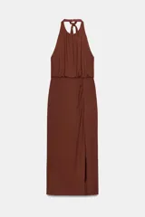 Vestido midi color marrón, con cuello halter que se anuda en la nuca, escote drapeado y frunces en el delantero. La falda es recta y presenta una abertura lateral.