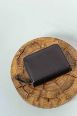 Billetera chica de cuero marrón con cierre de cremallera y logo de la marca grabado en el frente.