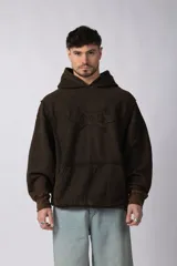 Buzo canguro marrón con capucha, calce oversize, confeccionado en frisa de algodón con lavado gastado y aplique cosido en el pecho.