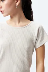 Remera color beige de punto acanalado con silueta relajada y manga corta raglán. El detalle de ruedo con terminación ondulada le aporta un aire fresco y juvenil.