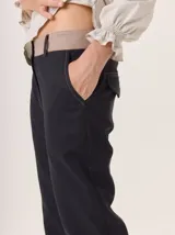 Pantalón de vestir color marrón, corte cigarette (pierna angosta) con tajo en el bajo. Presenta una cintura elástica ancha de color beige claro.