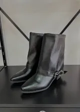 Botas de caña media negras de cuero sintético, con punta fina, taco bajo y correa con hebilla metálica alrededor del tobillo.
