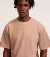 Remera color beige de corte boxy, con escote redondo y mangas cortas. Confeccionada en tejido acanalado de algodón y poliéster.