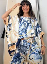 Blusa de satén color blanco con estampado floral en tonos azules y detalles de cadenas doradas. Diseño holgado con mangas cortas amplias y cuello redondo. Incluye cinturón marrón con hebilla dorada.