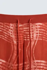Pantalón relaxed fit de punto ligero tejido en hilatura de algodón color ladrillo con estampado a cuadros difuminados en blanco. Cintura elástica ajustable con cordón y bolsillos laterales.