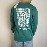 Buzo verde con cuello redondo y mangas largas. Estampado en la espalda con la frase "Chase Waves" y un diseño abstracto en blanco.