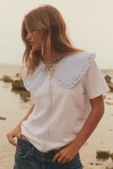 Camiseta blanca de manga corta con cuello bobo de tela a cuadros vichy celeste y blanco con bordes bordados. El cuello tiene lazos finos del mismo tejido.