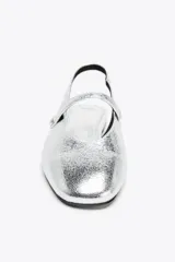 Zapato tipo bailarina destalonada plateada con efecto metalizado, punta redonda y tira delantera con aplique metálico.