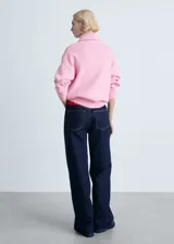 Sweater de punto rosa con cuello alto y cierre de cremallera roja. Diseño recto y manga larga.