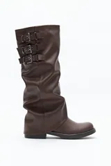 Bota de caña alta confeccionada en poliuretano con diseño de efecto fruncido y puntera redondeada. Presenta tres hebillas metálicas decorativas en el lateral superior de la caña y taco bajo.