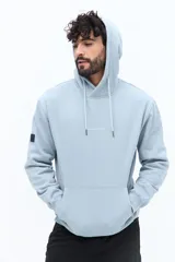 Canguro de algodón color celeste claro, con capucha ajustable mediante cordones trenzados blancos y bolsillo canguro frontal. Presenta un pequeño texto estampado en el pecho.