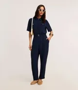 Camisa color beige de tela airflow, con cuello camisero, mangas cortas con detalle de pliegue, bolsillos con solapa en el pecho y cierre frontal con botones metalizados.