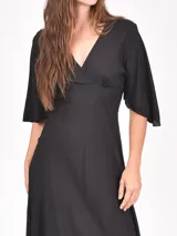 Vestido largo negro con escote cruzado en V y mangas tres cuartos. La falda es larga y fluida.