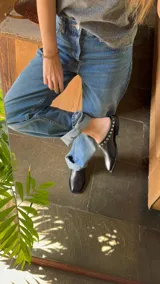 Mules de cuero color marrón con punta cuadrada y detalle de tachas doradas.