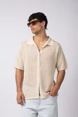 Camisa color crema tejida en algodón con calado aireado, de manga corta, cuello bowling y botones al tono.