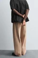 Pantalón de jean color beige, de corte ancho y tiro medio, con cinco bolsillos, efecto lavado y cierre frontal con cremallera y botón.