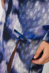 Vestido largo con estampado abstracto en tonos azules, violetas y grises. Tiene cuello mao con abertura en forma de gota, mangas largas acampanadas con detalle de botón en los puños, espalda abierta, tajo frontal y flecos en el ruedo.