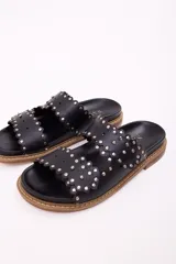 Sandalia tipo mule de mujer, color dorado metalizado, con dos tiras anchas superpuestas con borde festoneado y tachas doradas. La suela es gruesa y de color marrón claro.