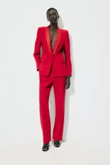 Blazer roja de corte recto, con cuello smoking de satén negro, mangas largas con hombreras, bolsillos frontales con solapa y cierre frontal con un botón.