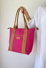 Bolso tipo tote de lona color fucsia con asas de cuero marrón, bolsillo interno y externo.
