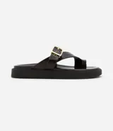 Sandalias planas de PU color marrón oscuro, con tira entre los dedos y tira ancha sobre el empeine con hebilla dorada ajustable.