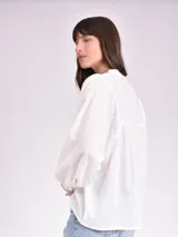 Camisa blanca de manga larga con bordado negro en el cuello y puños, con botones frontales.