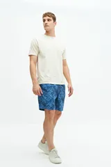 Short de baño largo azul con estampado abstracto de hojas en tonos azules más claros. Posee cintura elástica con cordón de ajuste gris, bolsillos laterales y un bolsillo trasero.