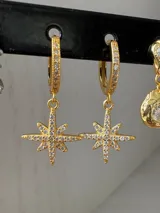 Aros dorados tipo argolla con incrustaciones de strass y dije colgante de estrella de ocho puntas con incrustaciones de strass.