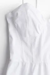 Vestido corto blanco de popelina de algodón, con breteles finos que se atan en moño, escote corazón y falda acampanada con volado en el ruedo.