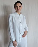 Camisa blanca de mangas largas con cuello alto con volados y botones marrones.