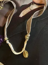 Collar con cinta de seda color beige y marrón, con cuentas doradas y medalla religiosa dorada.