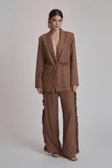 Blazer marrón con solapas de muesca, cierre frontal con lazo y mangas largas. Presenta volados a lo largo de las costuras laterales del pantalón a juego.